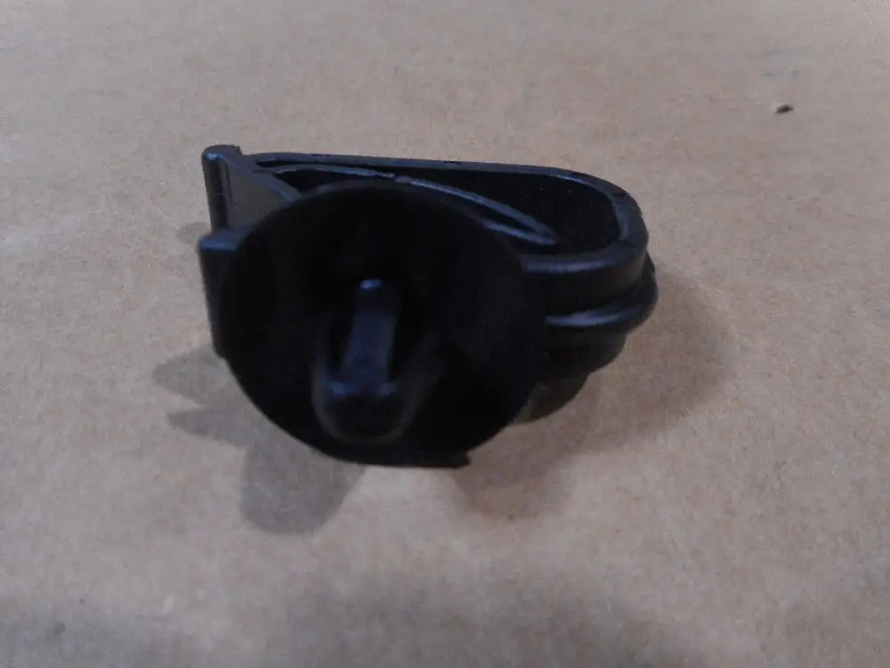 Schwarze Kabelklemme zur Befestigung, möglicherweise von Remeha, auf braunem Untergrund abgebildet. Das Produkt ist in einer seitlichen Position dargestellt.